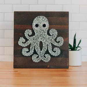 Puede incluir: Un pulpo de arte de cuerda blanco con ojos negros sobre un fondo de madera marrón oscuro.