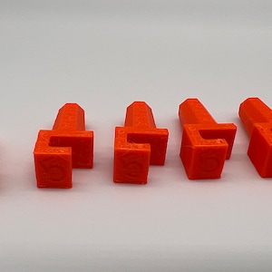 May include: Six orange plastic pieces with a square base and a raised top. The pieces have a small, raised, rectangular opening on the top.