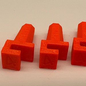 May include: Six orange plastic pieces with a square base and a rectangular top. The pieces have a small opening on the top.