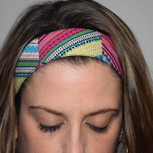 May include: A colorful patterned headband with pink, blue, green, and yellow accents. The headband is made of fabric and is worn on the forehead.