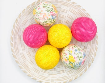 May include: Six fabric-covered Easter eggs in a white wicker basket. The eggs are in shades of pink, yellow, and white with floral patterns.