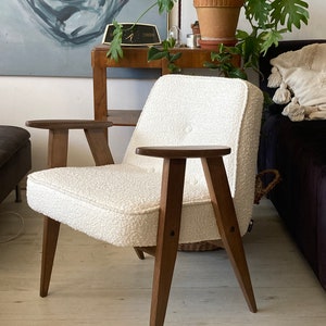 May include: A white armchair with a fluffy, textured fabric upholstery. The chair has a wooden frame with four legs and two armrests. The chair is sitting on a light wood floor.