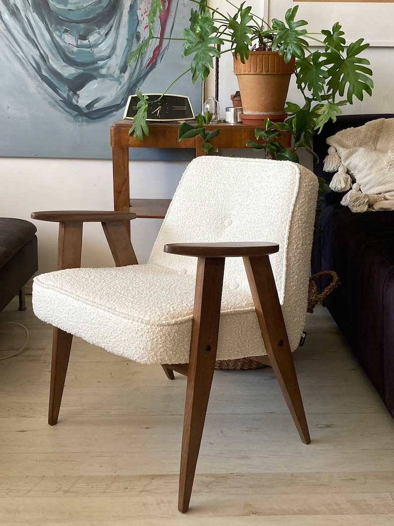 May include: A white armchair with a fluffy, textured fabric upholstery. The chair has a wooden frame with four legs and two armrests. The chair is sitting on a light wood floor.