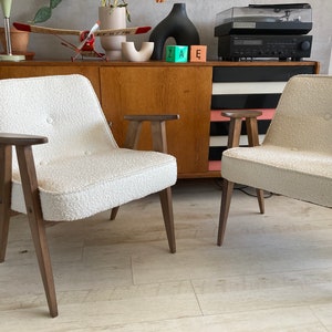May include: Two white chairs with wooden legs and arms. The chairs have a textured fabric upholstery and are positioned in front of a wooden cabinet with black and white stripes.