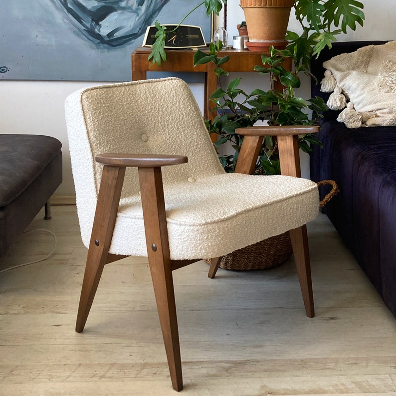 May include: A white armchair with a tufted back and wooden legs. The chair has a button detail on the back and is sitting on a wooden floor.