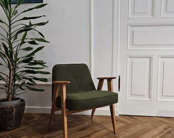 May include: A dark green armchair with wooden legs and arms, sitting on a wood floor with a herringbone pattern. A potted plant is in the background.