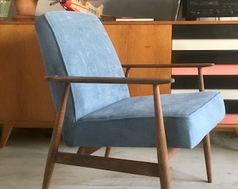 May include: A light blue armchair with wooden legs and arms. The chair is upholstered in a soft, textured fabric. The chair is sitting on a light wood floor.