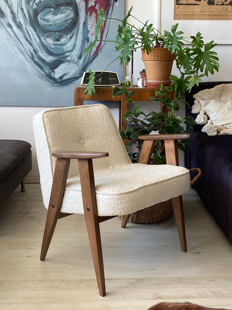 May include: A white armchair with a textured fabric upholstery and wooden legs. The chair has a button tuft on the back and a single button on the armrest.