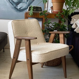 May include: A white armchair with a textured fabric upholstery and wooden legs. The chair has a button detail on the back and wooden armrests.