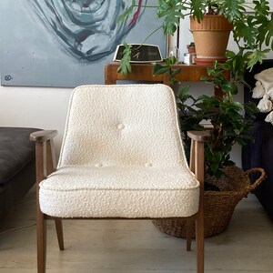 May include: A white armchair with a tufted back and seat, wooden arms, and dark brown legs. The chair is sitting on a wooden floor.