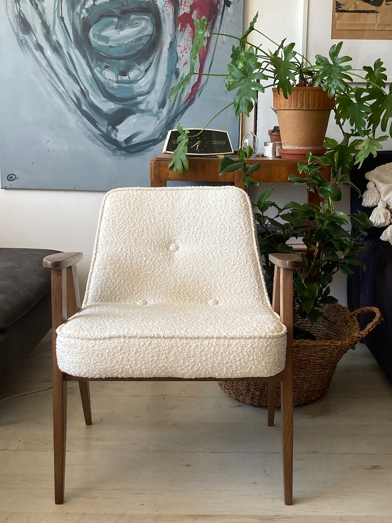May include: A white armchair with a tufted back and seat, wooden arms, and dark brown legs. The chair is sitting on a wooden floor.