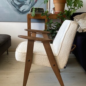 May include: A white armchair with a textured fabric upholstery and wooden legs. The chair has a simple, mid-century modern design.