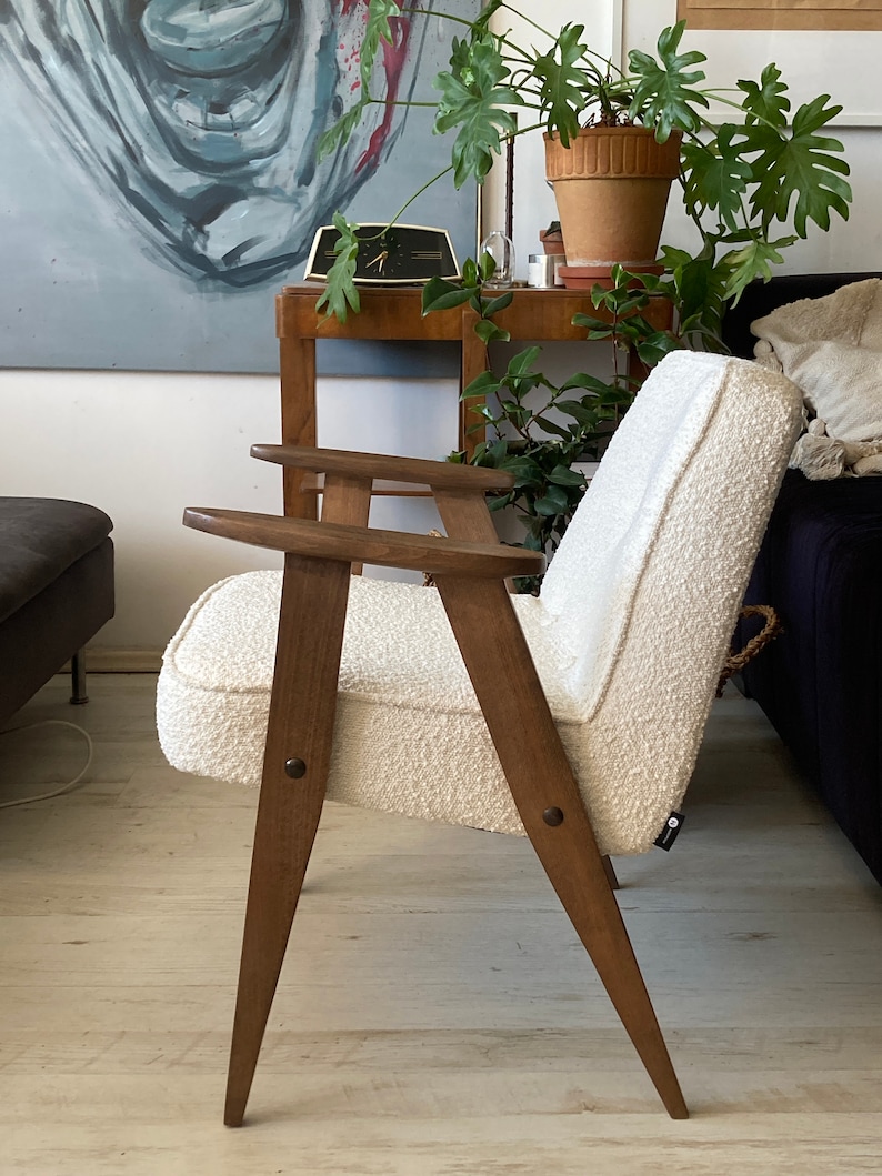May include: A white armchair with a textured fabric upholstery and wooden legs. The chair has a simple, mid-century modern design.