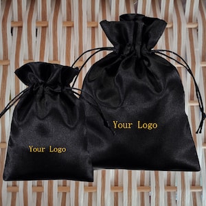 May include: Two black satin drawstring bags with gold text that reads "Your Logo".