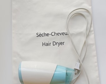 Pode incluir: Um secador de cabelo branco e azul com uma bolsa com cordão a condizer. A bolsa tem a inscrição "Sèche-Cheveu, Hair Dryer". O secador de cabelo tem uma pega branca e um bocal azul.
