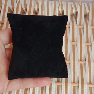May include: A black velvet jewelry box or ring pillow. The pillow is small and square, and is sitting on a woven surface.