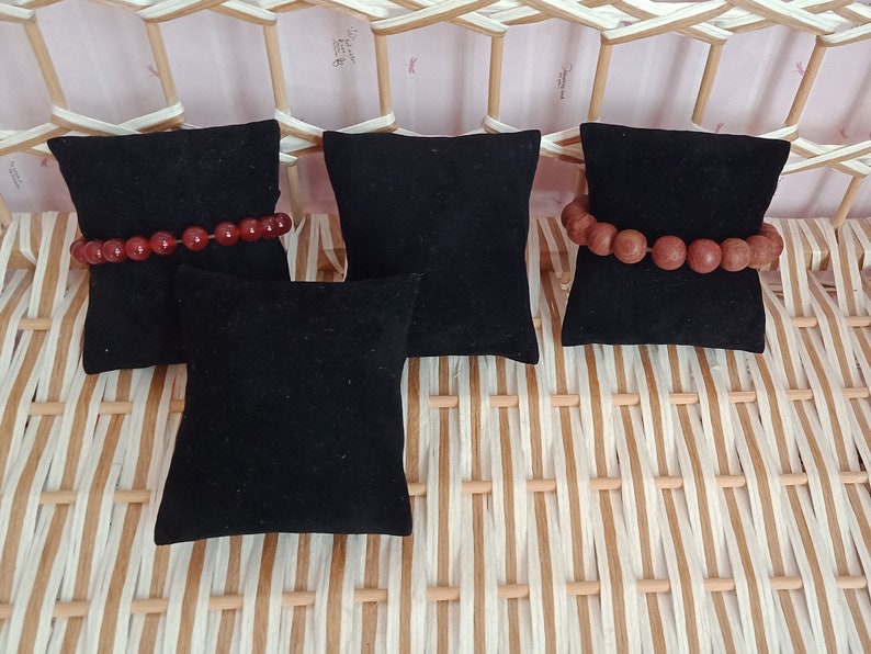 May include: Four black velvet ring display cushions, two with red gemstone bracelets on top.