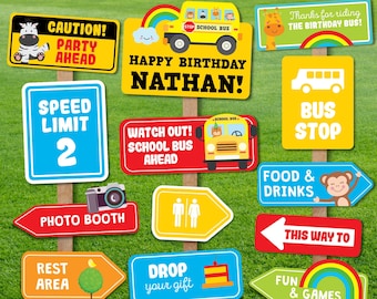 May include: A set of 12 colorful signs with various phrases and images, perfect for a school bus themed birthday party. The signs feature a school bus, a zebra, a monkey, a giraffe, and other fun illustrations. The signs include phrases like "Happy Birthday Nathan!" and "Speed Limit 2".