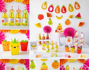 May include: A colorful party table setting with a fruit theme. The table is decorated with fruit-shaped paper cutouts, fruit-themed cupcake toppers, and a cake with fruit-shaped decorations. The table also has a sign that says "Happy Birthday Mollie".