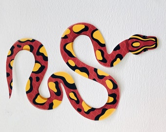 May include: A red and yellow snake with a black outline, curled into a figure eight shape. The snake has a patterned design with spots and stripes.