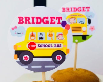 May include: Yellow school bus cupcake toppers with animal characters, a stop sign, and the text "STOP SCHOOL BUS". The toppers also feature the name "BRIDGET" in pink letters.