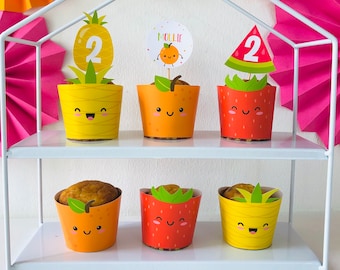 May include: A two-tiered white stand with six decorated cupcakes. The cupcakes are decorated with fruit themes, including pineapple, strawberry, and orange. The cupcakes are topped with a number two and a name tag that says "Mollie".
