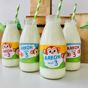 May include: Four glass milk bottles with green and white striped straws. Each bottle has a colourful label with a cartoon monkey and the text "Aaron turns 3".