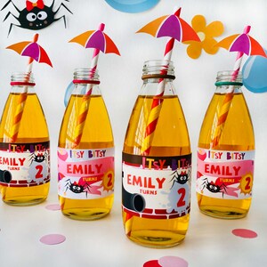 May include: Four clear glass bottles with orange juice and colorful straws. Each bottle has a personalized label with the name "Emily" and the text "Itsy Bitsy" and "Turns 2". The labels also feature a cartoon spider and other colorful designs.