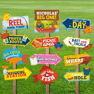 May include: A set of 12 colourful, illustrated signs for a fishing themed party. The signs feature phrases like "Reel Good Times", "Big Catch Guaranteed", "Weighing Station", "Keep Calm & Fish", "Catch of the Day", "Bait and Tackle", "Fisherman's Wharf", "Fishing Hole", "Live Worms", "Picnic Area", "Photo Booth", and "Nicholas' Big One".