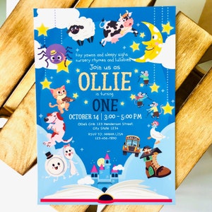 May include: A blue and white invitation for a first birthday party for a baby named Ollie. The invitation features a book with a castle and animals on the cover. The text on the invitation reads "Join us as Ollie is turning One. October 14 | 3:00 - 5:00 PM. Ollie's Crib 123 Henderson Street, City State 1234. RSVP TO: MAMA LISA 123-456-7890."