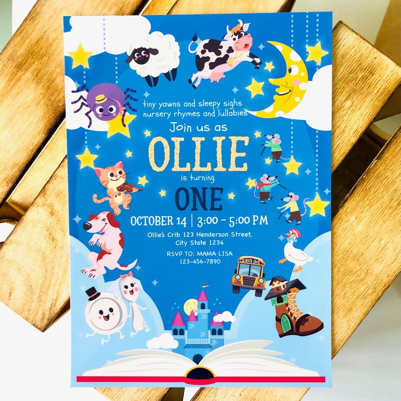 May include: A blue and white invitation for a first birthday party for a baby named Ollie. The invitation features a book with a castle and animals on the cover. The text on the invitation reads "Join us as Ollie is turning One. October 14 | 3:00 - 5:00 PM. Ollie's Crib 123 Henderson Street, City State 1234. RSVP TO: MAMA LISA 123-456-7890."