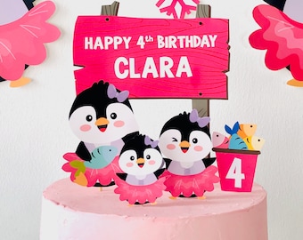 May include: A pink and white cake with a penguin family theme. The cake is decorated with a wooden sign that says "Happy 4th Birthday Clara" and penguin figurines holding fish. The cake is also decorated with a snowflake and a bucket of fish.