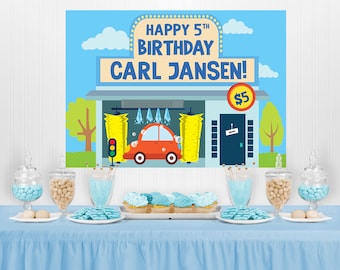 May include: A blue and yellow car wash themed birthday party backdrop with the text "Happy 5th Birthday Carl Jansen!" and a red car in the car wash. The backdrop is set up on a table with blue tablecloths, candy jars, and cupcakes.