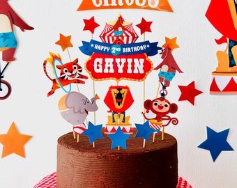 May include: A chocolate cake decorated with a circus theme. The cake features a variety of circus animals, including a lion, an elephant, a monkey, and a tiger. The cake also has a sign that says "Happy 2nd Birthday Gavin".