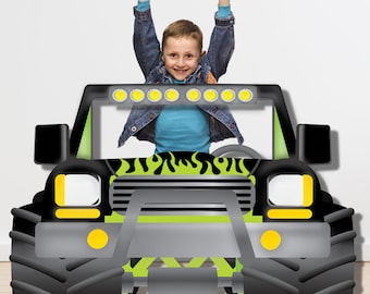 Puede incluir: Un recorte de cartón de camión monstruo negro y verde con un niño de pie en el asiento del conductor. El camión tiene neumáticos grandes, una parrilla, faros y un diseño de llamas verdes.