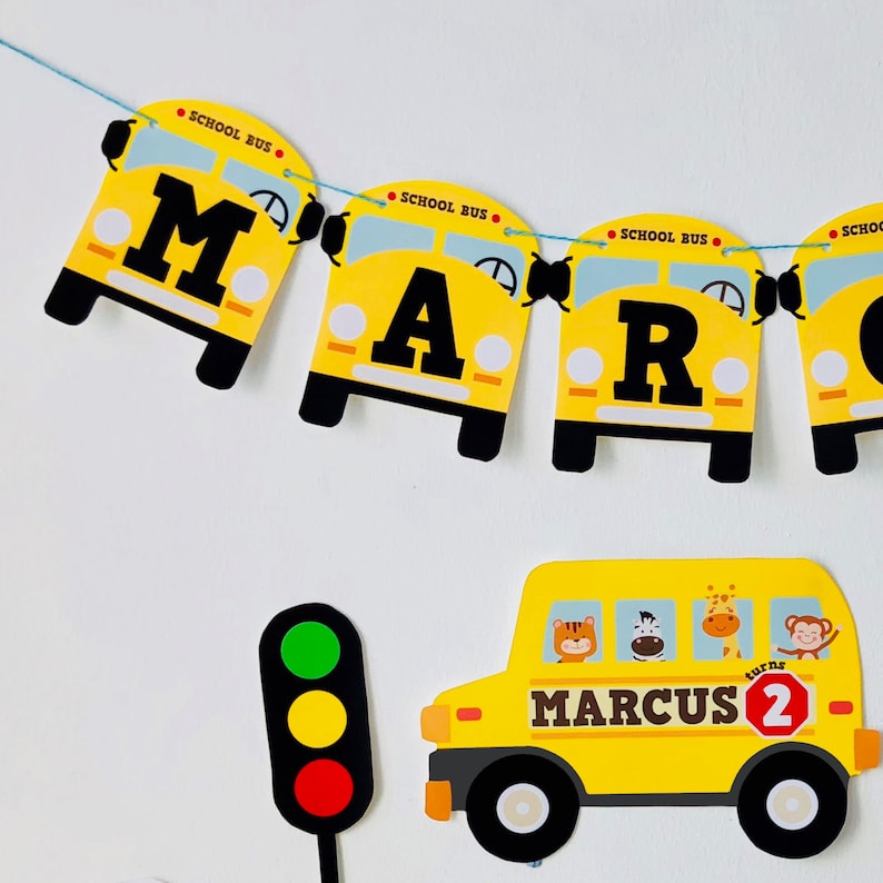 Wheels on the Bus personalised birthday banner spelling "MARCUS turns 2" with yellow school bus garland, animal characters, and traffic light party props
