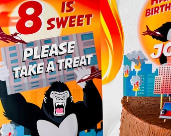 May include: A birthday party sign with a gorilla holding a sign that says "8 is sweet please take a treat". The sign is orange and blue with a cityscape background. 