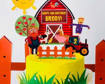 Puede incluir: Un pastel amarillo decorado con un granero rojo, un granjero, animales y un tractor. El granero tiene el texto "Happy 2nd Birthday Brody!" El pastel está rodeado de hierba verde.