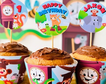 May include: Three chocolate cupcakes decorated with colorful cupcake wrappers featuring a clock, a monkey, and a snake. The cupcakes are topped with a chocolate frosting. Each cupcake has a small, round, colorful paper topper with a cartoon animal and the words "Happy Birthday" and "Jaxon".