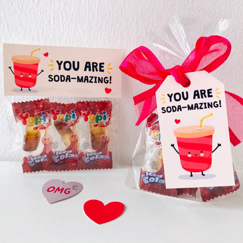 Pu&ograve; includere: Due sacchetti trasparenti di cellophane pieni di caramelle, ciascuno con un'etichetta che dice "YOU ARE SODA-MAZING!". Le borse sono legate con un nastro rosa. Sono presenti anche un cuore rosa e un adesivo a forma di cuore con la scritta "OMG".