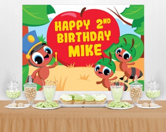 May include: A red apple with a bite taken out of it, with the text "Happy 2nd Birthday Mike" on it. There are three cartoon ants on the backdrop, one wearing a police hat, another wearing a green leaf hat, and the third wearing a green leaf hat. The backdrop is green and brown.