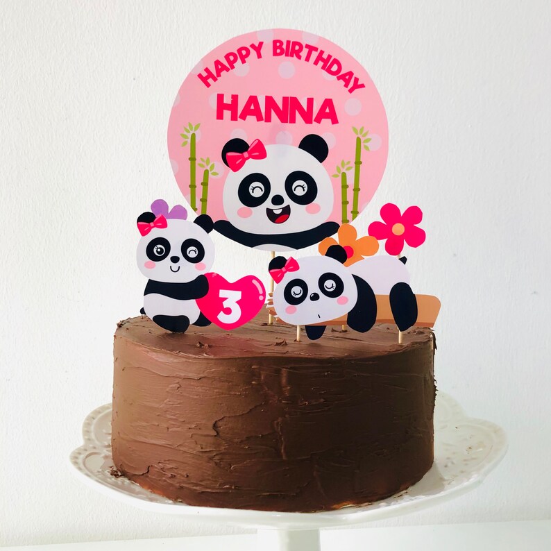 Op de afbeelding: Een chocoladetaart versierd met een roze en witte panda-taarttopper. De topper zegt "Happy Birthday Hanna" en heeft een nummer 3 erop.