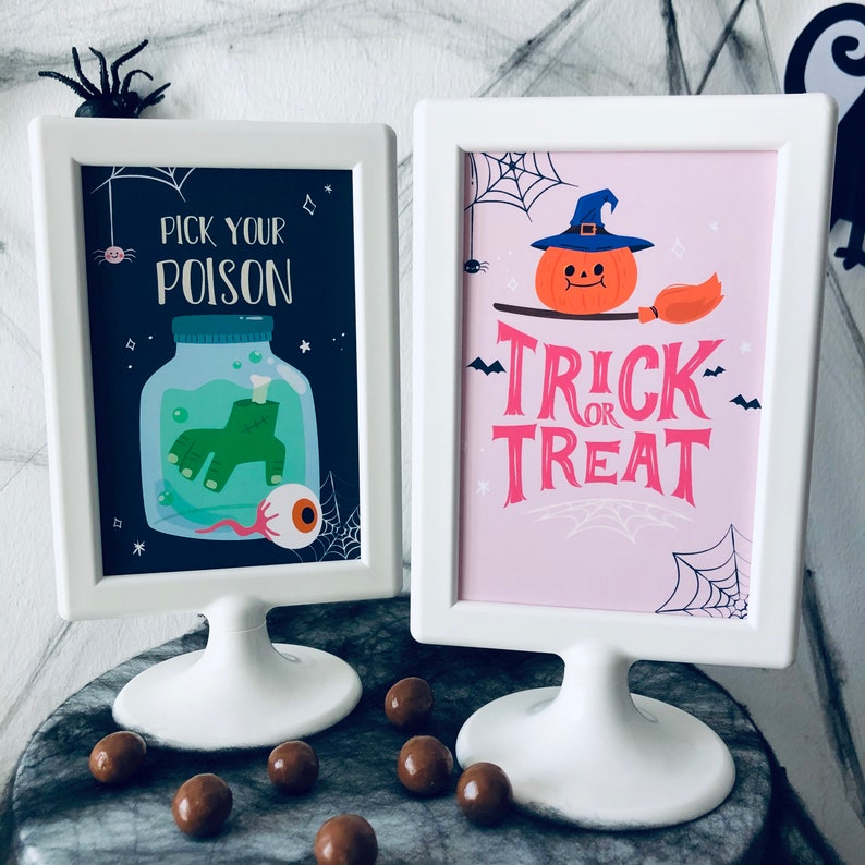 May include: Two white picture frames with black and pink Halloween themed images. The left frame has a green hand in a jar with an eyeball and the text "Pick your poison". The right frame has a pumpkin with a witch's hat and the text "Trick or Treat".