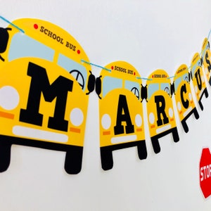 Close-up of Wheels on the Bus editable birthday banner garland with yellow school buses spelling MARCUS for toddler school bus themed party decoration