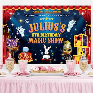 May include: A blue and red circus-themed backdrop with stars and the text "ABRACADABRA! PREPARE TO BE MYSTIFIED & AMAZED AT ***** JULIUS'S 5TH BIRTHDAY MAGIC SHOW!"  A table with pink and white candy jars, cupcakes, and pink and white candy on a pink tablecloth.