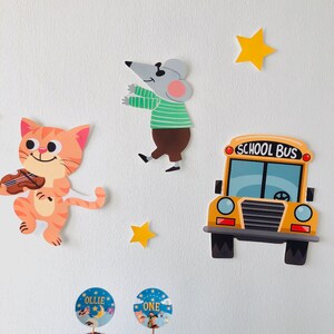 Op de afbeelding: Een set kleurrijke papieren uitsnijdingen met een viool spelende kat, een muis met een zonnebril, een gele schoolbus en twee gele sterren. De uitsnijdingen zijn op een witte achtergrond. De uitsnijdingen maken deel uit van een feestdecoratieset.