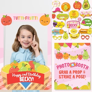 May include: A pink and white photo booth frame with a basket of fruit and the text "TUTTI-FRUTTI" and "Happy 2nd Birthday Becky!"  The frame is decorated with fruit-themed props, including a pear, an apple, a banana, a pineapple, and a watermelon. The text "PHOTOBOOTH" and "GRAB A PROP & STRIKE A POSE!" is also included.