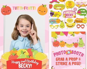 May include: A pink and white photo booth frame with a basket of fruit and the text "TUTTI-FRUTTI" and "Happy 2nd Birthday Becky!"  The frame is decorated with fruit-themed props, including a pear, an apple, a banana, a pineapple, and a watermelon. The text "PHOTOBOOTH" and "GRAB A PROP & STRIKE A POSE!" is also included.