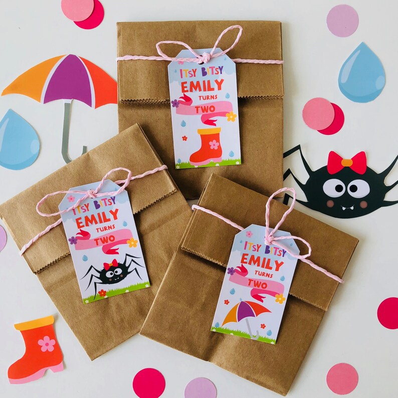 May include: Three brown paper bags with pink string and colorful gift tags that say "Itsy Bitsy Emily Turns Two" with different illustrations of a rain boot, a spider, and an umbrella.
