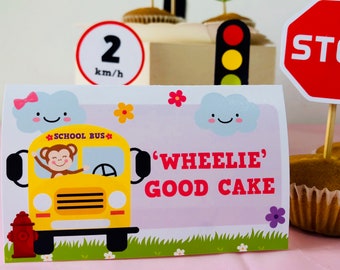 May include: A pink and purple cake topper with a cartoon monkey driving a yellow school bus. The text on the topper reads "SCHOOL BUS" and "'WHEELIE' GOOD CAKE".